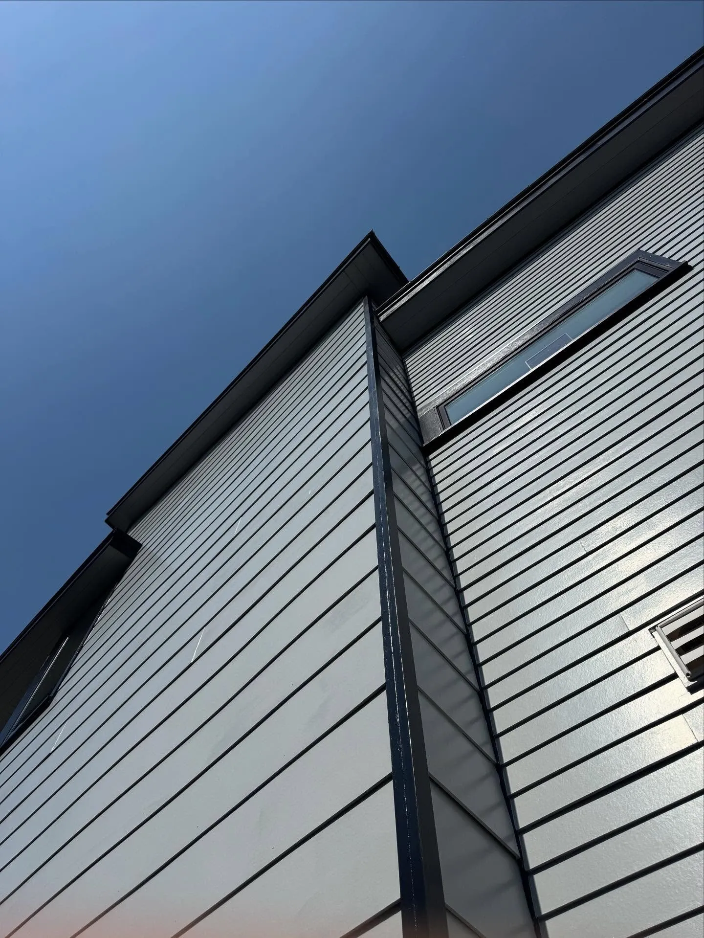 Looking up at freshly painted lap siding and trim against a blue sky