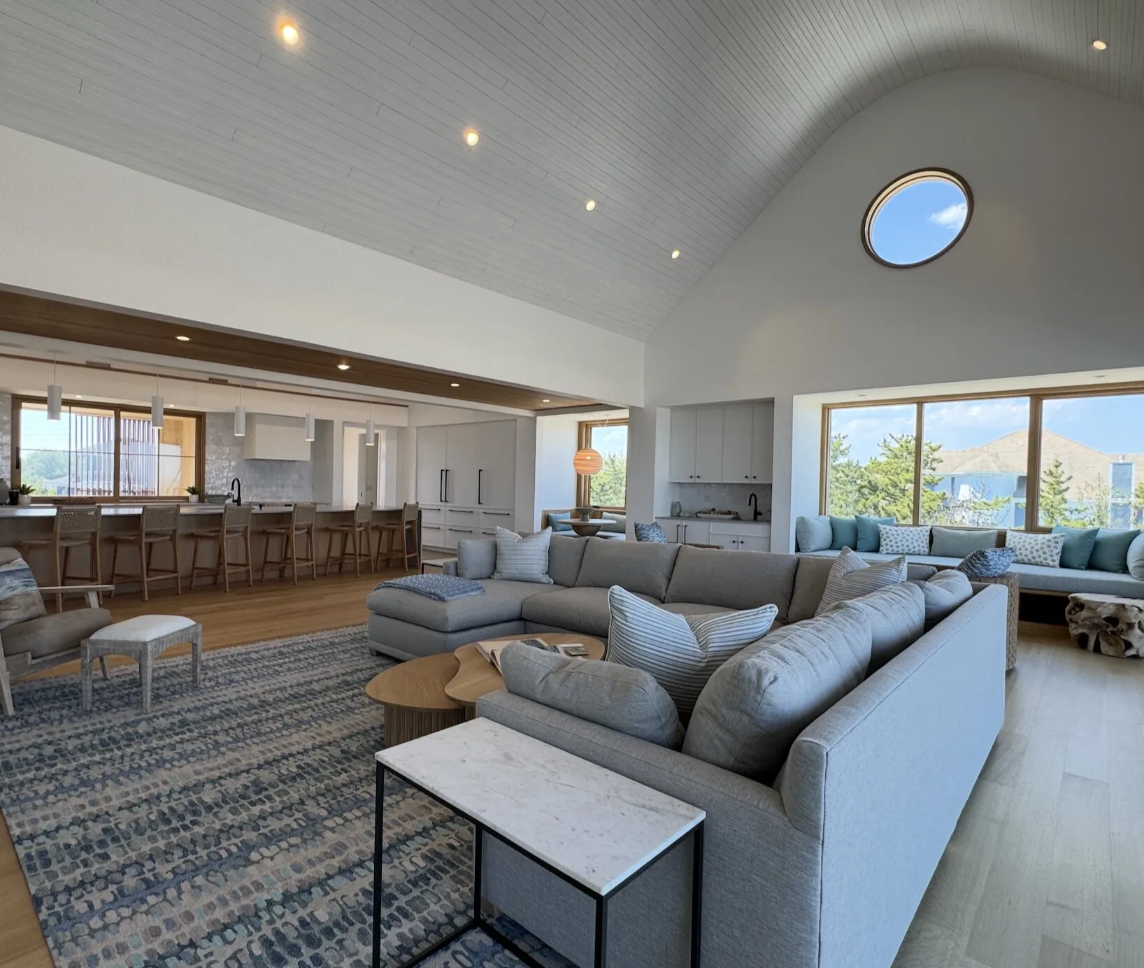 Bright great room with a vaulted white ceiling, porthole window and fresh white walls in a coastal home