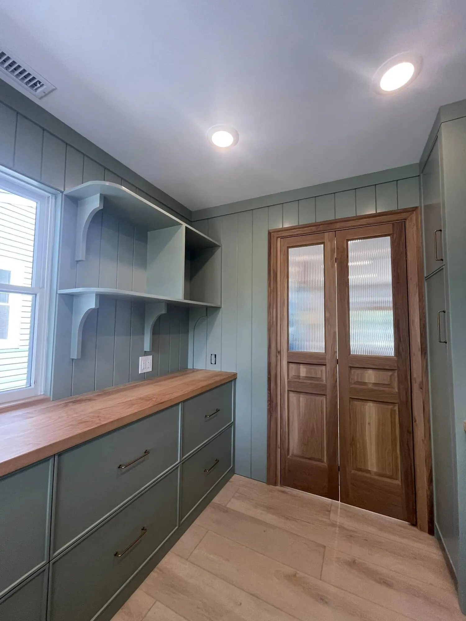 Mudroom built-ins painted green with open shelving and a stained wood door