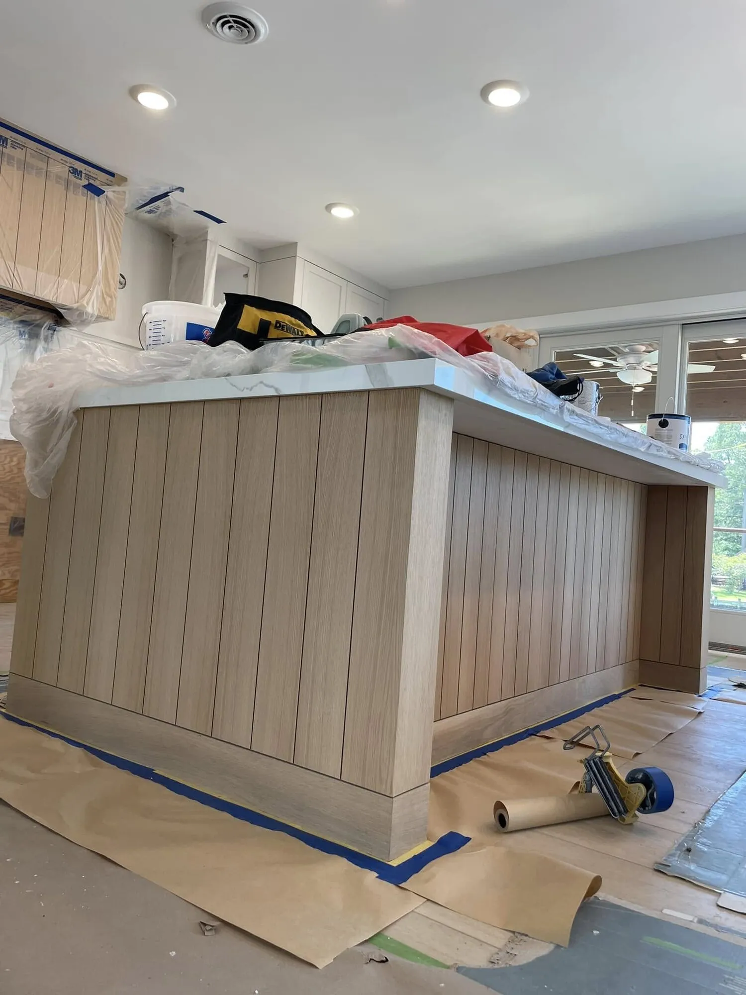 Kitchen island with vertical oak paneling being finished, floors fully protected