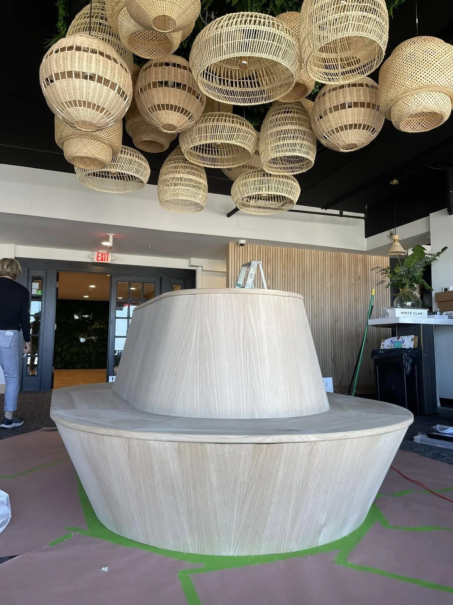 Round restaurant banquette in natural oak being finished under woven pendant lights