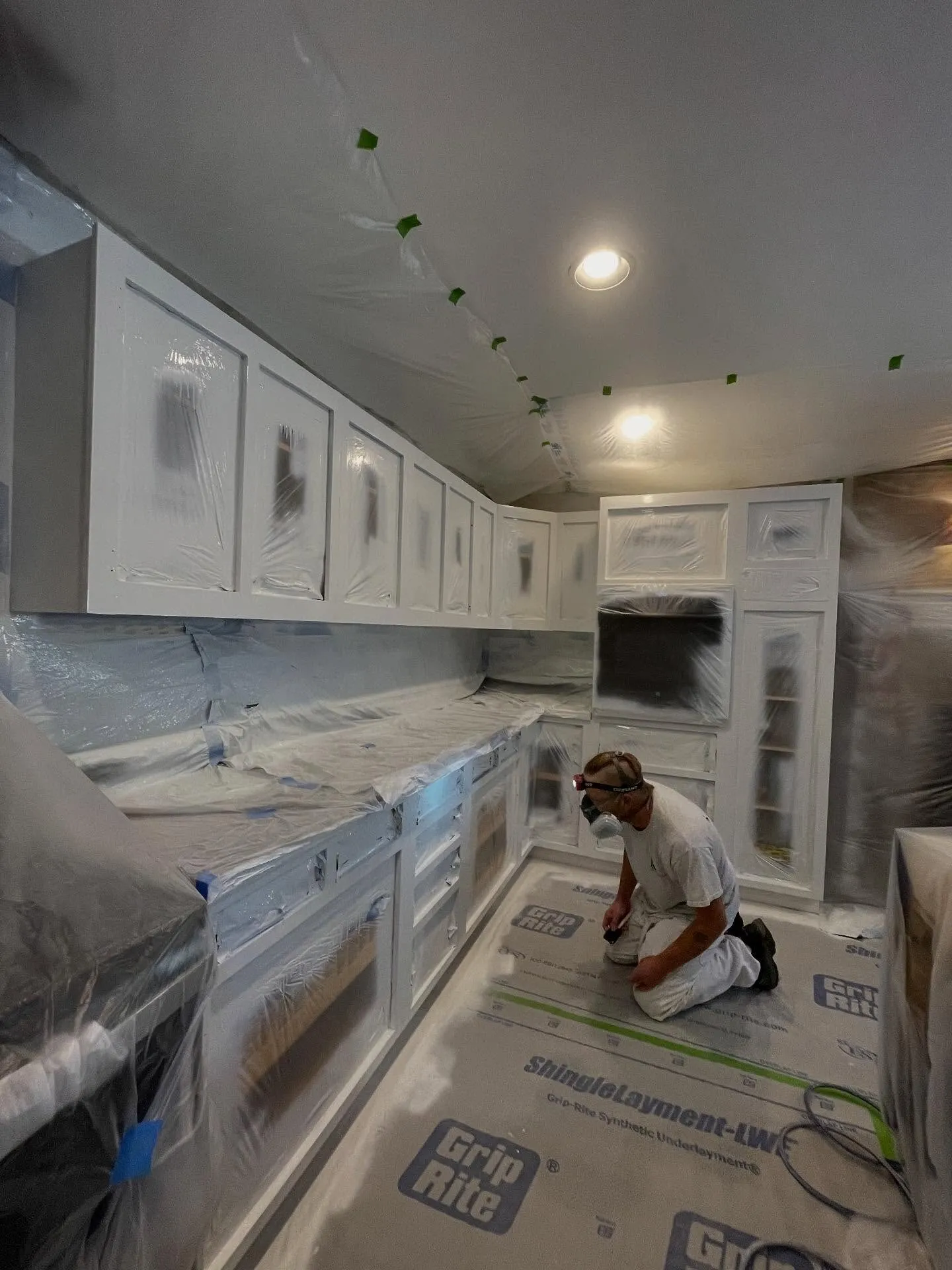 Painter spraying kitchen cabinets with counters and floors fully masked