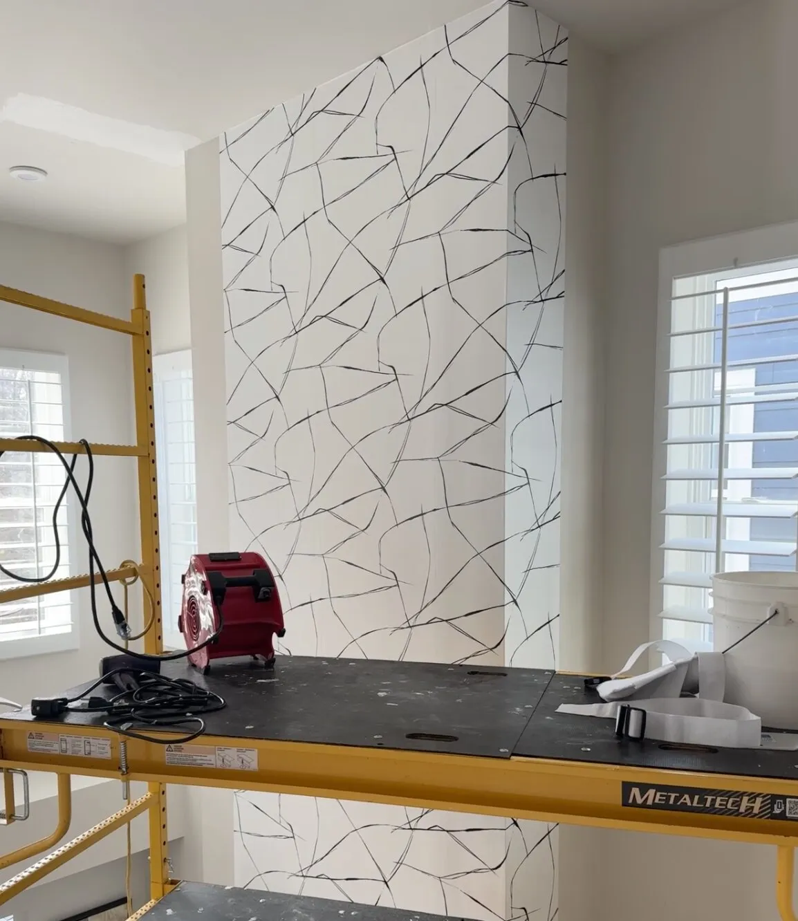 Graphic black-and-white wallpaper being hung on a tall accent wall from scaffolding
