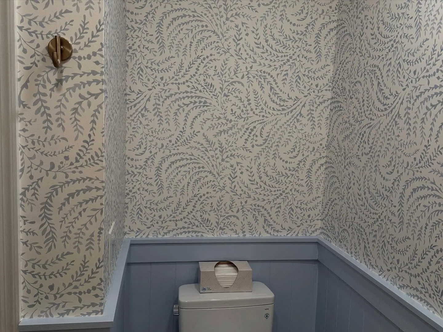Powder room with botanical wallpaper above painted blue wainscoting
