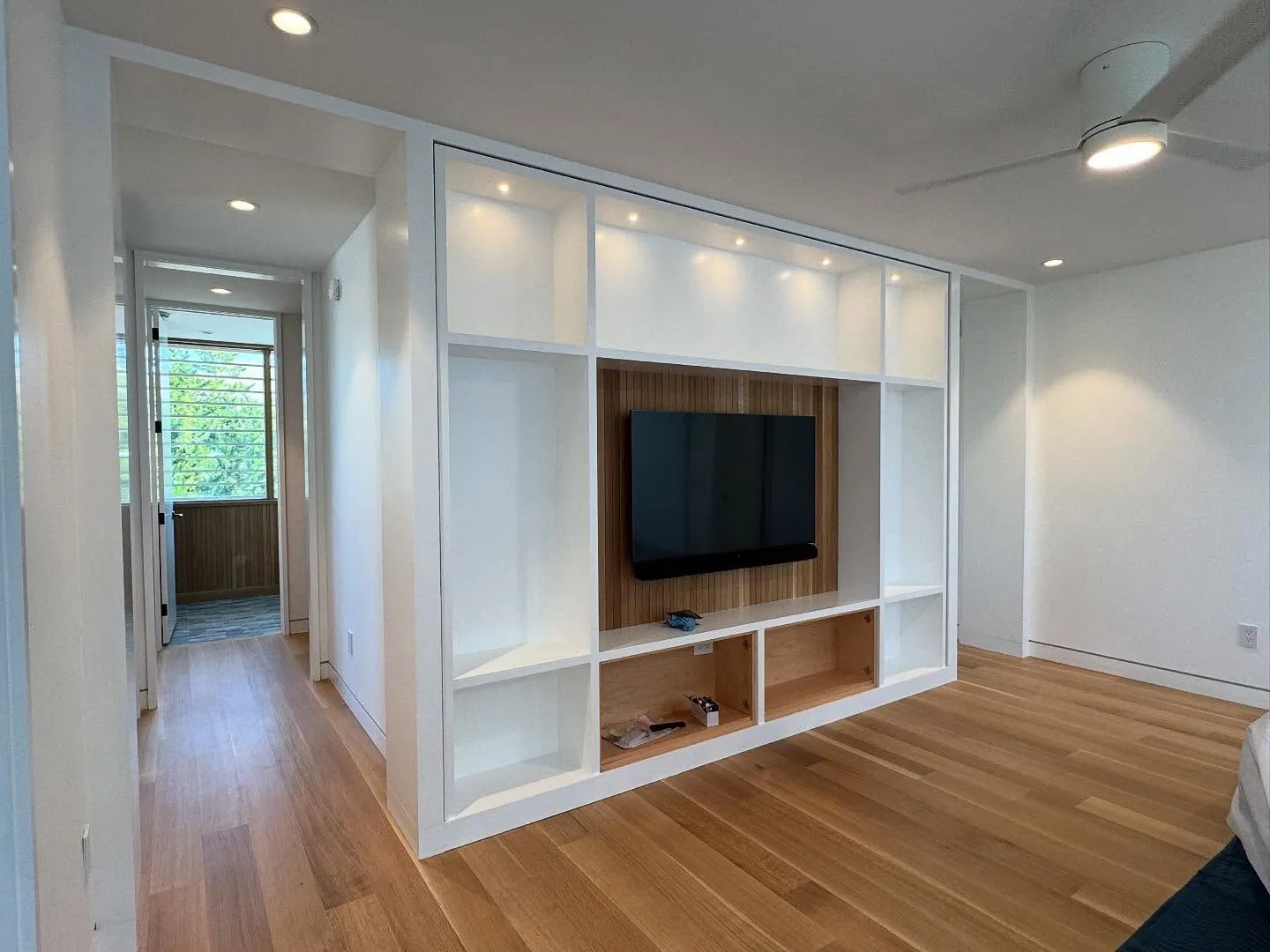 White built-in shelving wall with lighting and a wood-backed TV niche